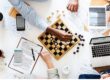 Professionals using a chessboard to represent strategic decision-making when comparing JBCC contracts, FIDIC contracts and NEC contracts.