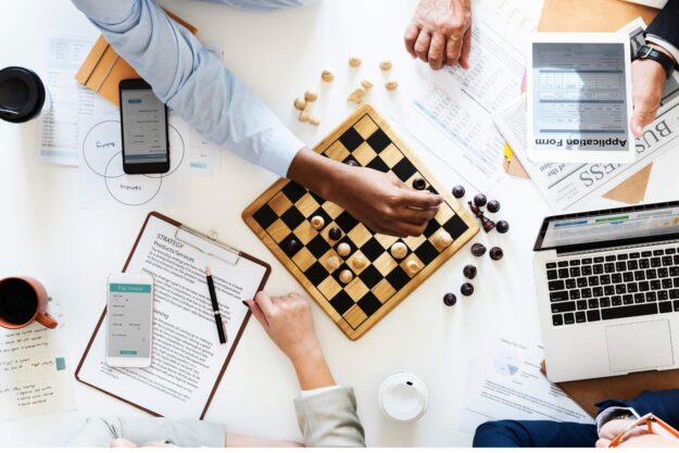 Untitled design – 2026-06-29T102548.809 Professionals using a chessboard to represent strategic decision-making when comparing JBCC contracts, FIDIC contracts and NEC contracts.